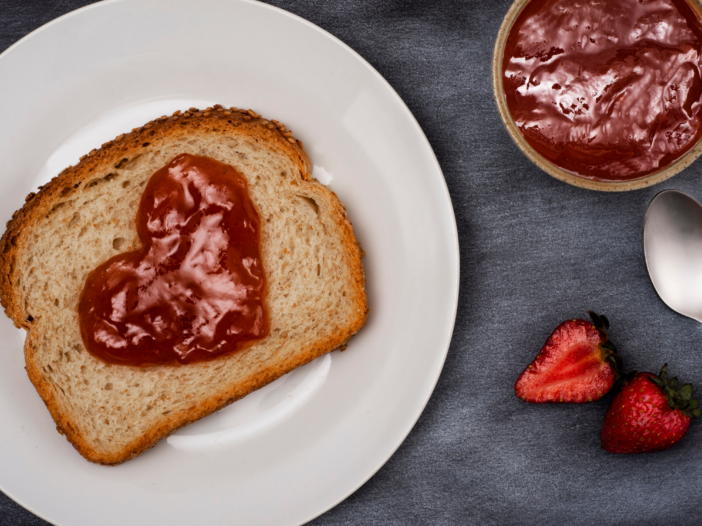 Piece of whole wheat toast with a heart drawn in strawberry jam on it