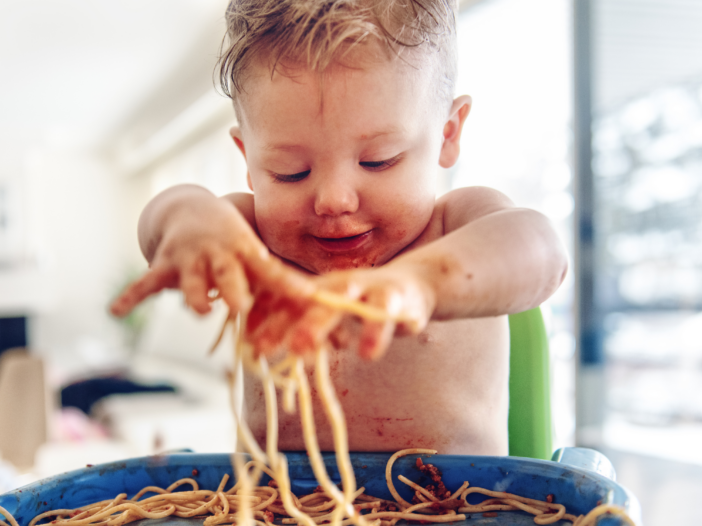 baby eating pasta in a high chair