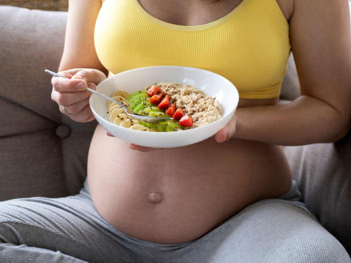 pregnant woman eating oatmeal topped with fresh fruit