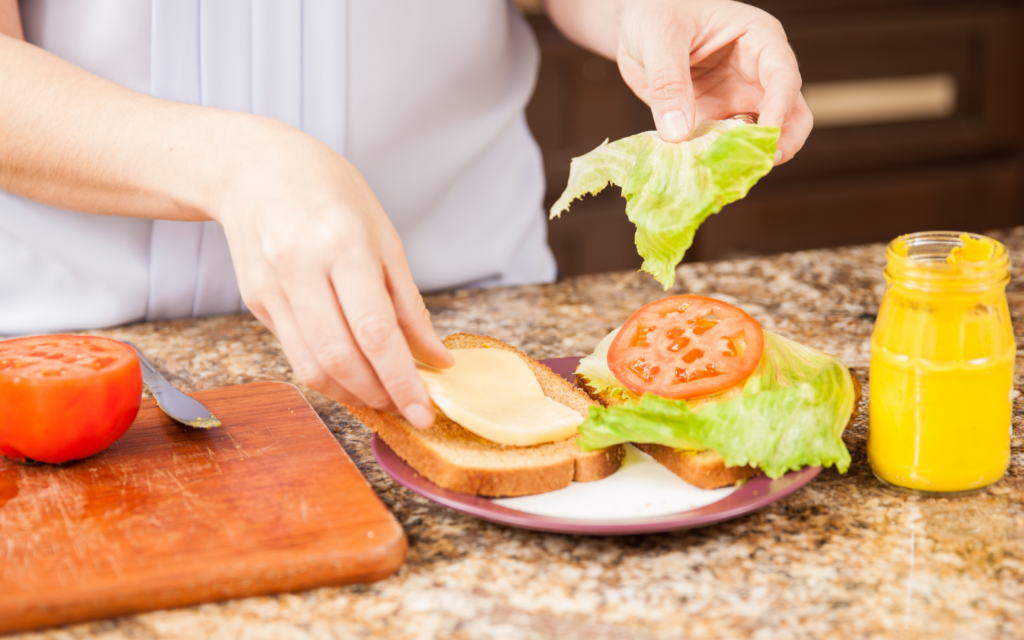 Hands making a sandwich topped with lettuce and tomato