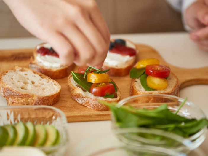 Woman topping crostini with herbs and tomatoes