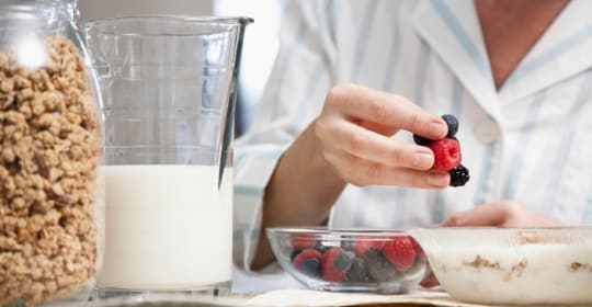 Woman adding fruit to her granola and yogurt bowl