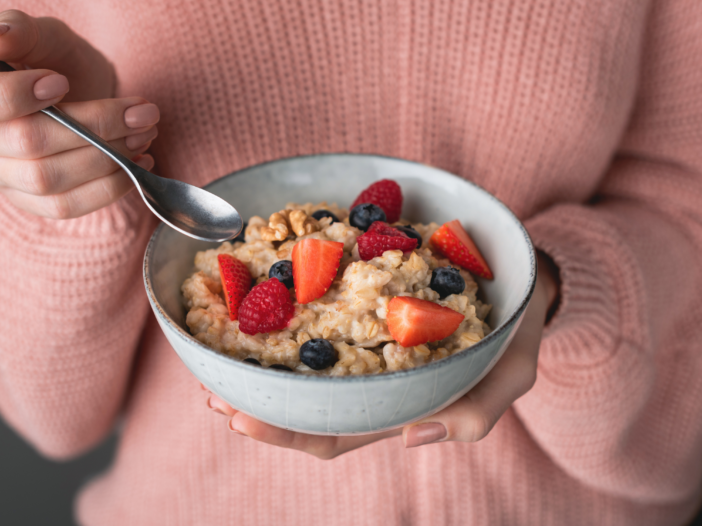 Woman holding a bowl of oatmeal topped with blueberries and strawberries